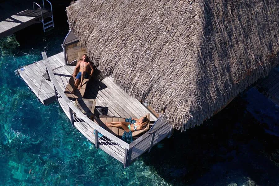 People lay on lounge chairs on an over-water deck at Manava Beach Resort & Spa Moorea People lay on lounge chairs on an over-water deck at Manava Beach Resort & Spa Moorea